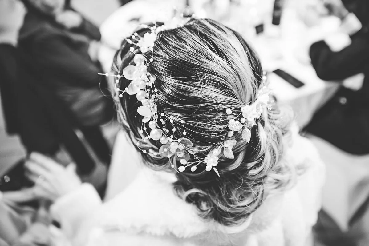 La coifure de la mariée ornée de sa parures de perles et plumes fines